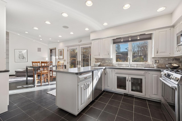 kitchen with dark tile patterned floors, a sink, a peninsula, dishwashing machine, and gas range