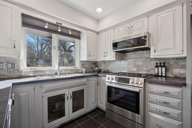 kitchen featuring dark tile patterned flooring, a sink, decorative backsplash, appliances with stainless steel finishes, and dark countertops