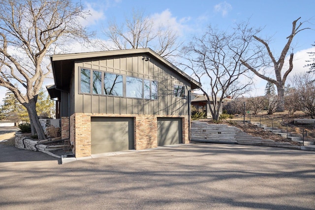 view of side of home featuring board and batten siding, aphalt driveway, an attached garage, and brick siding