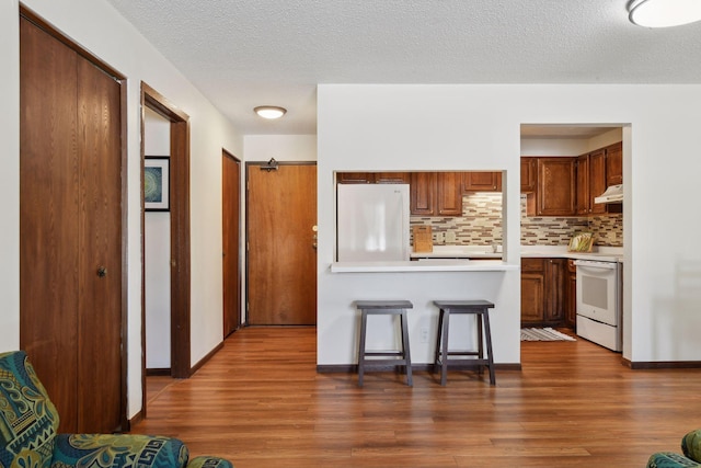 kitchen with a breakfast bar area, tasteful backsplash, light countertops, dark wood-type flooring, and white appliances