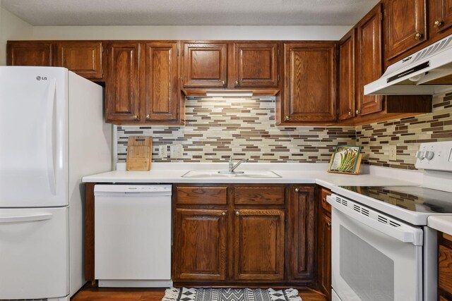 kitchen featuring white appliances, a sink, under cabinet range hood, and decorative backsplash