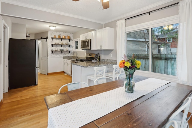 dining space featuring ceiling fan, crown molding, a barn door, baseboards, and light wood-style flooring