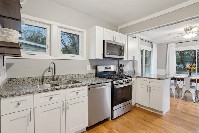 kitchen with light wood-type flooring, a sink, a peninsula, stainless steel appliances, and white cabinetry