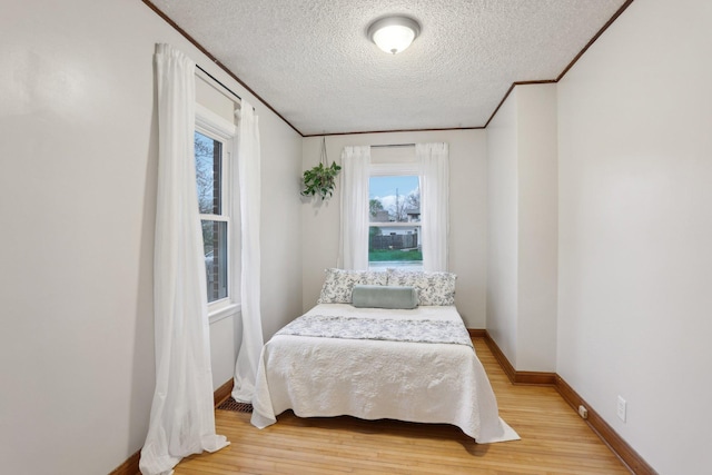bedroom with baseboards, multiple windows, light wood-style flooring, and a textured ceiling