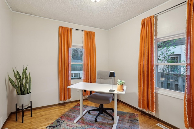 office featuring a textured ceiling, visible vents, a healthy amount of sunlight, and light wood finished floors