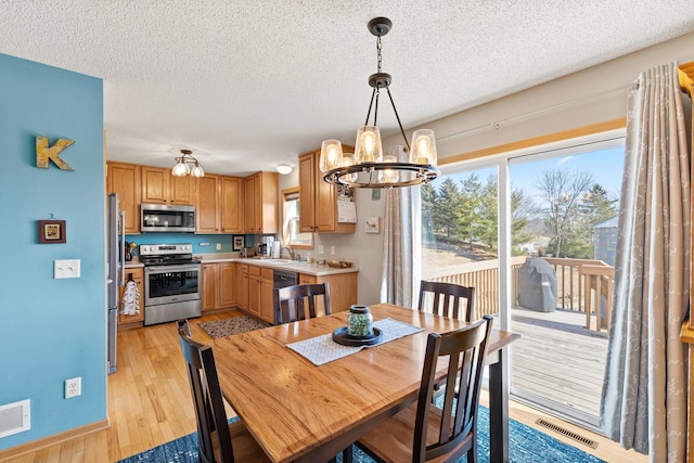 dining space featuring visible vents, a notable chandelier, light wood-style flooring, and a textured ceiling