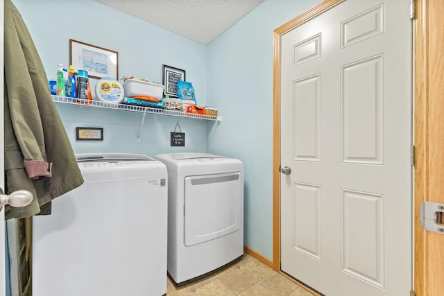 laundry area with laundry area, light tile patterned floors, baseboards, washing machine and clothes dryer, and a textured ceiling