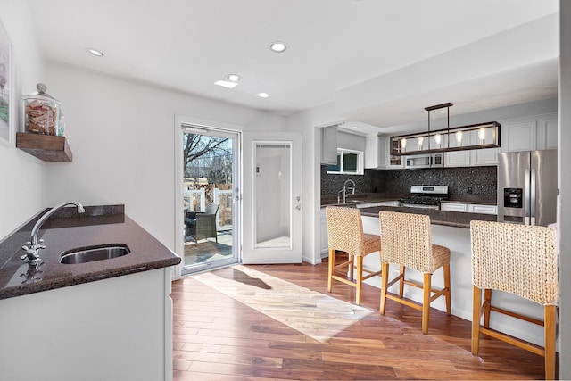 kitchen featuring a kitchen breakfast bar, a sink, stainless steel appliances, light wood finished floors, and decorative backsplash