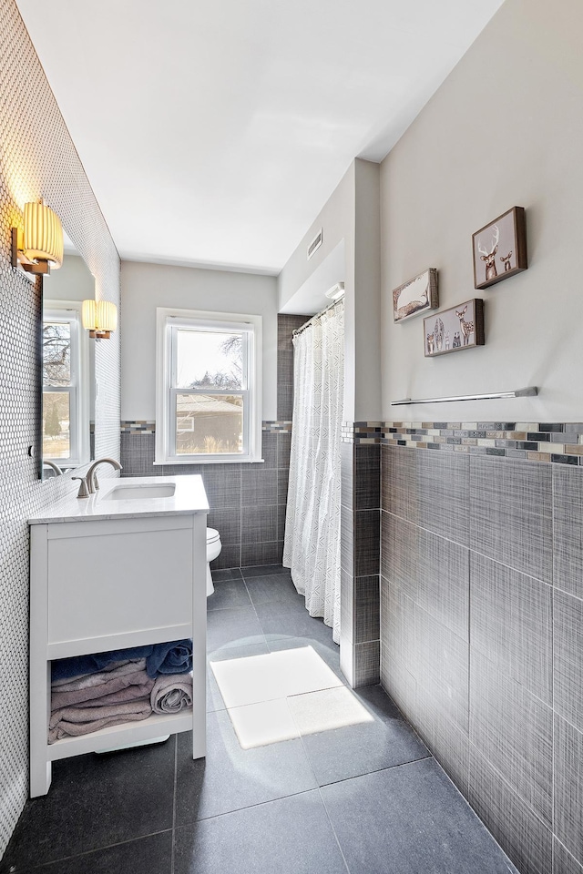 full bath featuring a wealth of natural light, vanity, tile walls, and toilet