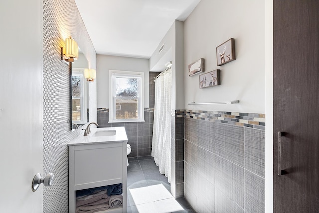 bathroom with visible vents, toilet, tile walls, vanity, and tile patterned flooring