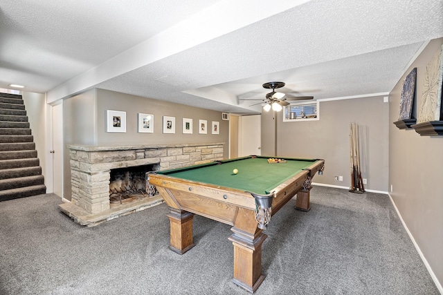 recreation room with a textured ceiling, ceiling fan, carpet, and a stone fireplace