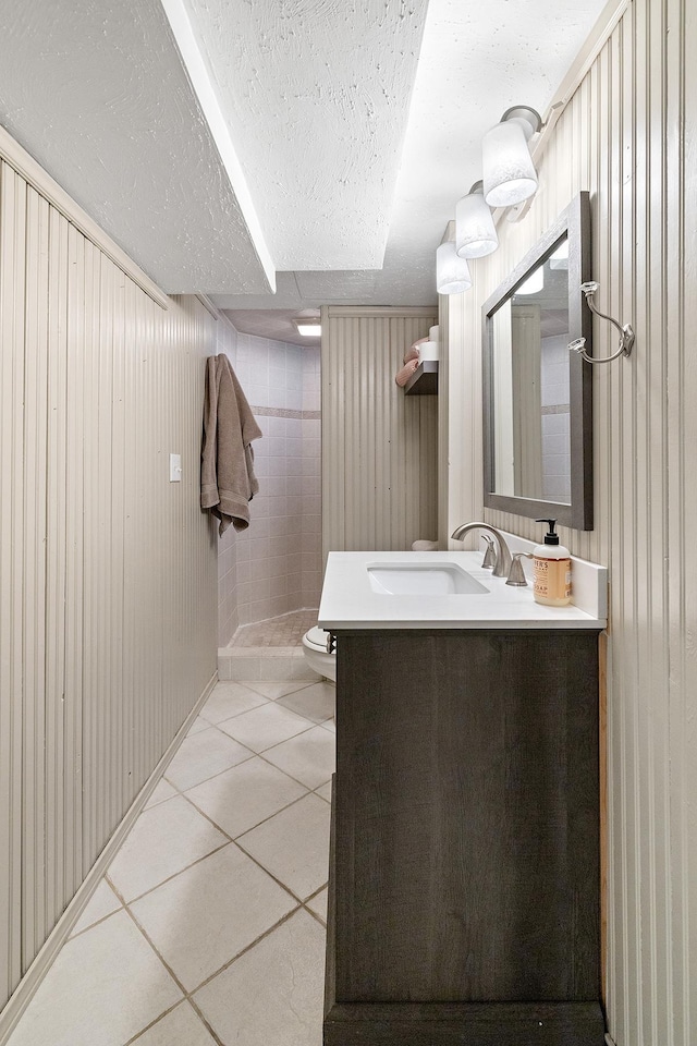 full bathroom featuring a tile shower, toilet, a textured ceiling, vanity, and tile patterned flooring