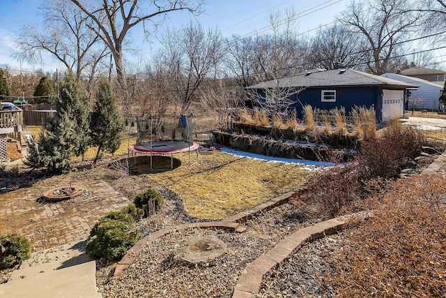 view of yard with a trampoline, a garage, and fence