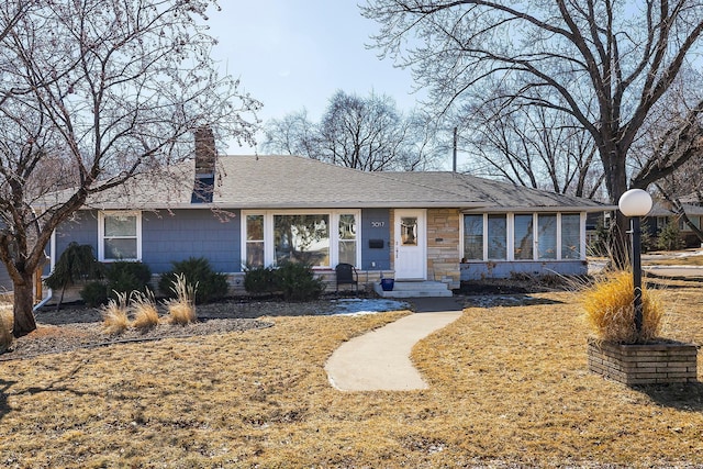 ranch-style house with a shingled roof, stone siding, and a chimney