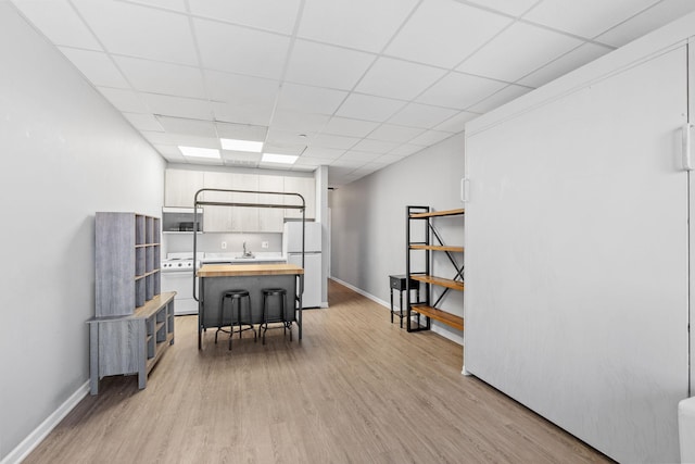 interior space featuring washer / dryer, sink, a drop ceiling, and light hardwood / wood-style flooring