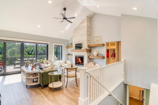 living room featuring high vaulted ceiling, light hardwood / wood-style floors, a large fireplace, and ceiling fan