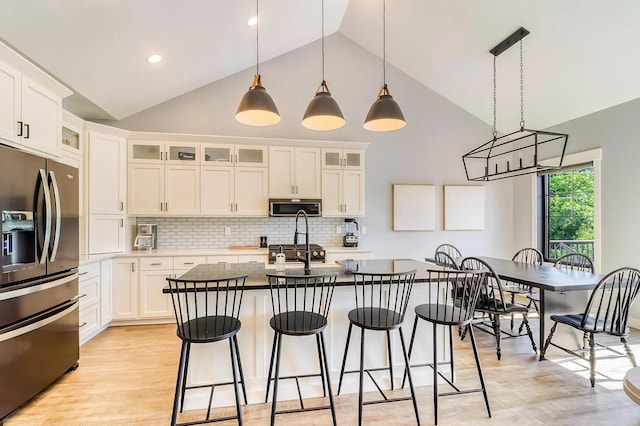 kitchen featuring stainless steel refrigerator with ice dispenser, a breakfast bar, white cabinetry, an island with sink, and pendant lighting