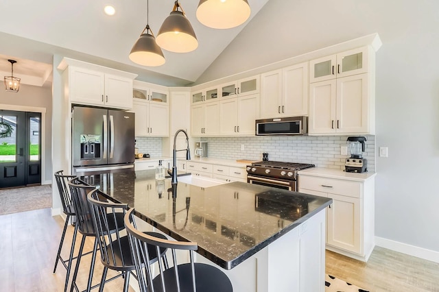 kitchen featuring sink, dark stone countertops, stainless steel appliances, a center island with sink, and decorative light fixtures