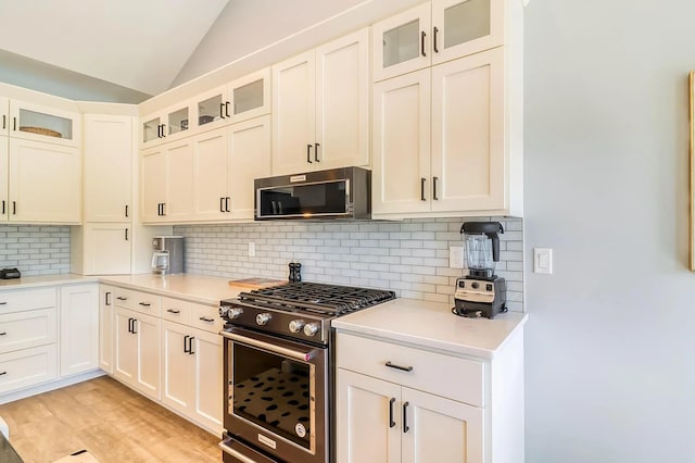 kitchen with lofted ceiling, decorative backsplash, stainless steel gas range oven, and white cabinets