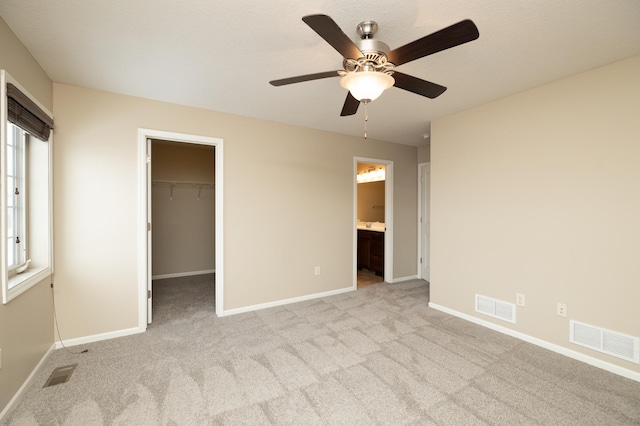 unfurnished bedroom featuring a walk in closet, a closet, ceiling fan, light carpet, and ensuite bathroom