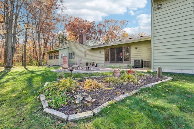 back of house featuring a chimney, central AC, a lawn, and a patio area