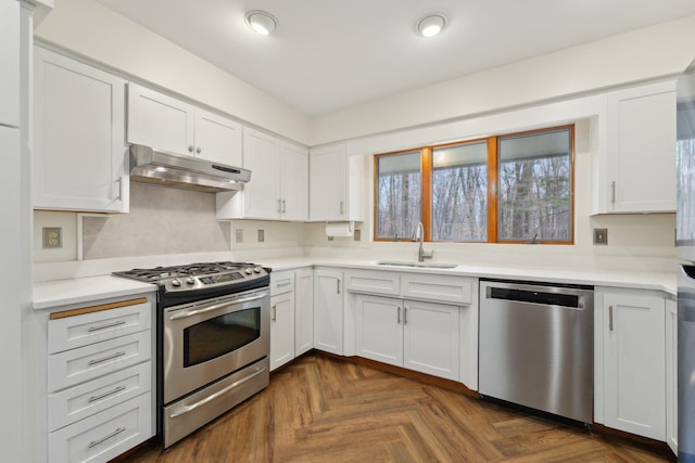 kitchen with under cabinet range hood, a sink, white cabinets, light countertops, and appliances with stainless steel finishes