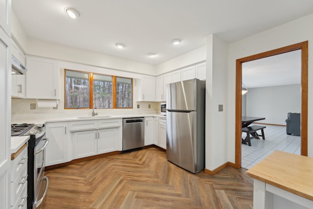 kitchen with a sink, baseboards, white cabinets, light countertops, and appliances with stainless steel finishes