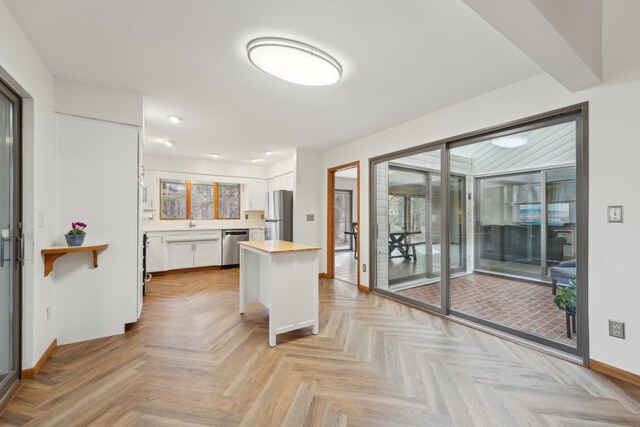 kitchen with baseboards, white cabinets, a center island, stainless steel appliances, and wooden counters