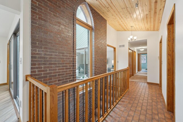 hallway featuring wood ceiling, brick wall, visible vents, and a healthy amount of sunlight