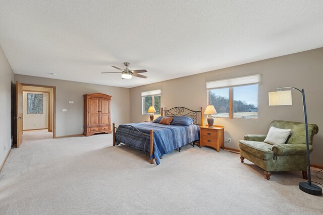 bedroom with light carpet, a textured ceiling, baseboards, and a ceiling fan