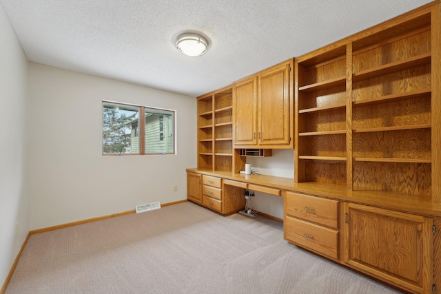 unfurnished office with light colored carpet, visible vents, built in study area, a textured ceiling, and baseboards