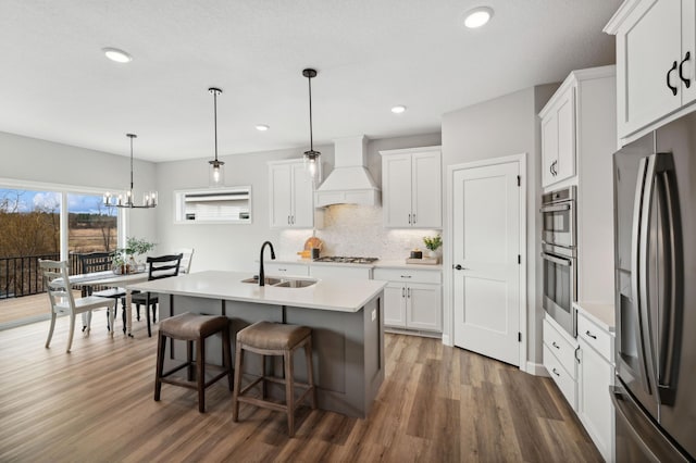 kitchen with sink, custom exhaust hood, pendant lighting, stainless steel appliances, and white cabinets