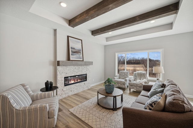 living room featuring beamed ceiling, a stone fireplace, and light hardwood / wood-style floors