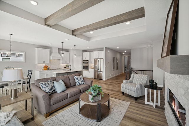 living room featuring beamed ceiling, an inviting chandelier, sink, and hardwood / wood-style flooring