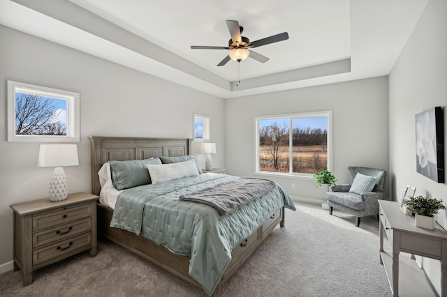 bedroom featuring a tray ceiling, light colored carpet, and ceiling fan