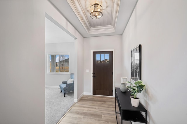 foyer featuring a tray ceiling, crown molding, light hardwood / wood-style flooring, and a chandelier