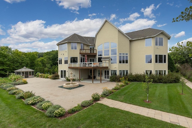 back of house featuring a balcony, stucco siding, a patio, a lawn, and a gazebo