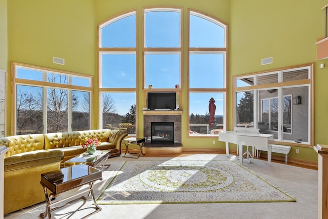 living area with a high ceiling, a healthy amount of sunlight, a glass covered fireplace, and visible vents