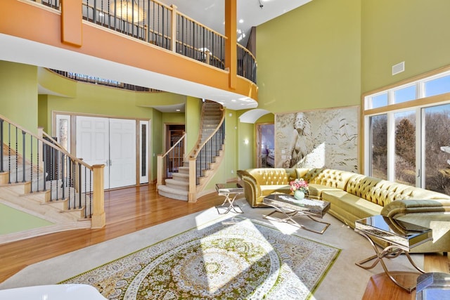 living room with stairs, wood finished floors, arched walkways, a towering ceiling, and visible vents