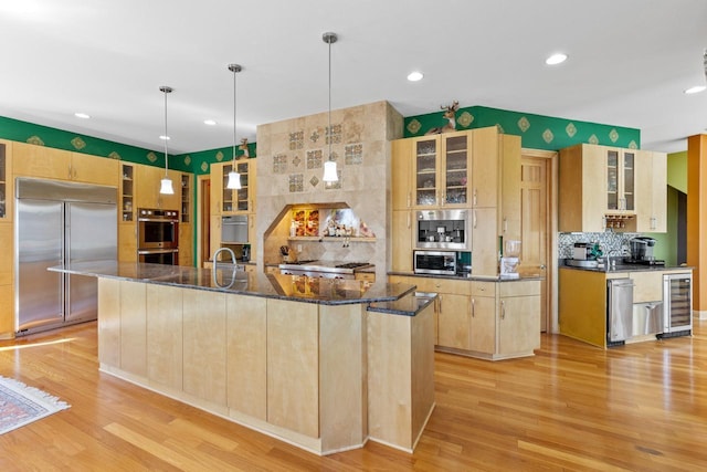 kitchen with beverage cooler, light brown cabinetry, light wood-style floors, a spacious island, and appliances with stainless steel finishes