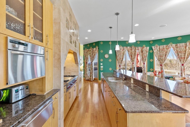 kitchen featuring wallpapered walls, a large island, a sink, light wood-type flooring, and appliances with stainless steel finishes