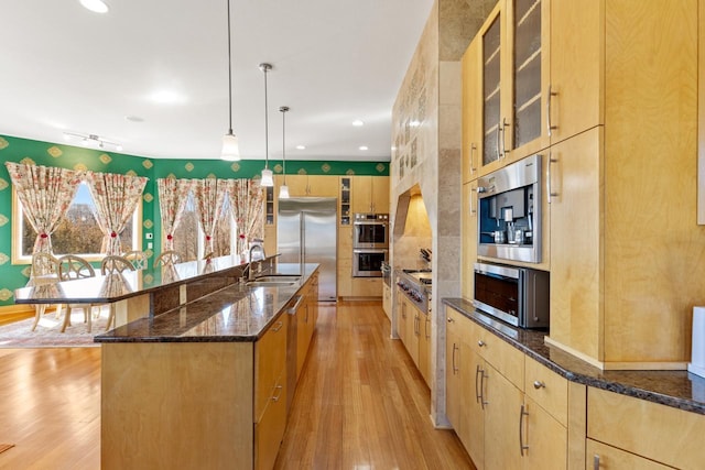 kitchen featuring light wood finished floors, light brown cabinets, stainless steel appliances, and a sink