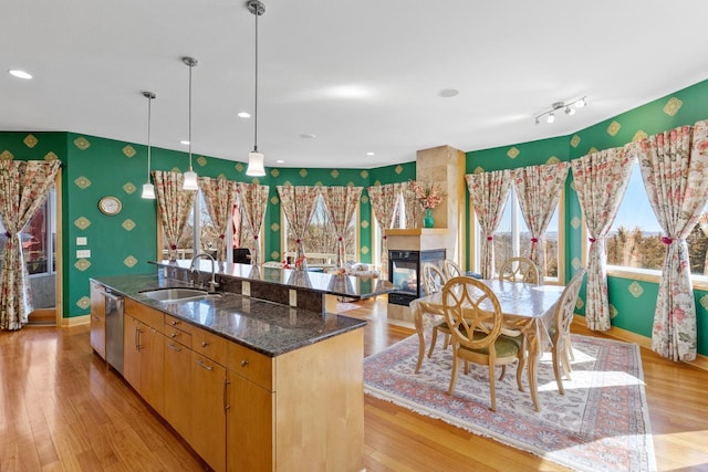 kitchen with a sink, wallpapered walls, light wood-style floors, dishwasher, and baseboards