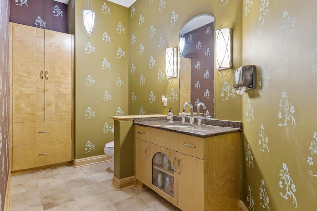 bathroom with wallpapered walls, baseboards, vanity, and toilet