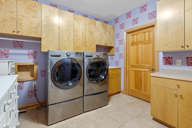 clothes washing area with cabinet space, wallpapered walls, washing machine and clothes dryer, and light tile patterned floors
