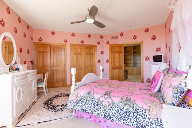 bedroom featuring wallpapered walls, multiple closets, visible vents, and a ceiling fan
