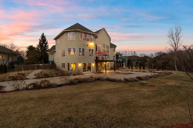back of property at dusk featuring stucco siding, a yard, and a balcony