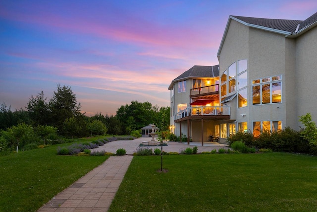 19115 Vogel Farm Trl, Eden Prairie, MN 55347 - back of house at dusk featuring a patio, stucco siding, a balcony, and a yard