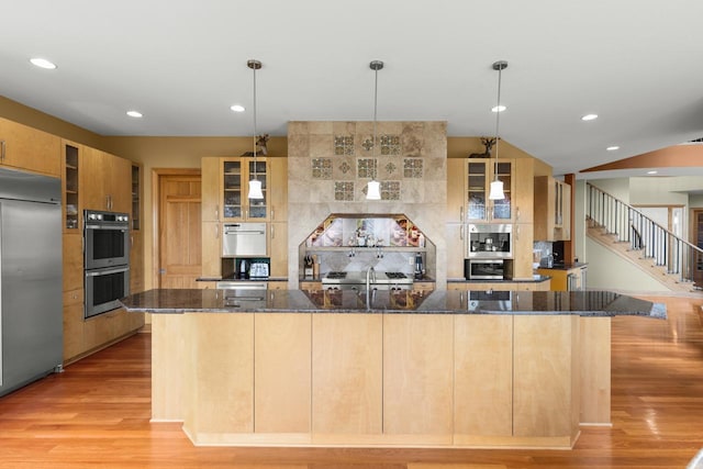 19115 Vogel Farm Trl, Eden Prairie, MN 55347 - kitchen with stainless steel appliances, light wood-type flooring, a spacious island, dark stone countertops, and glass insert cabinets