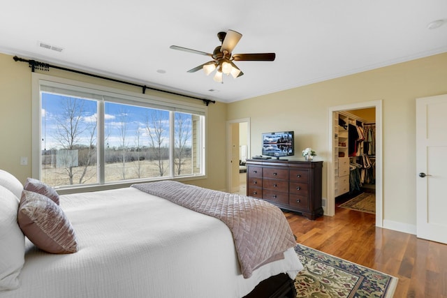 bedroom featuring a ceiling fan, visible vents, wood finished floors, a spacious closet, and ornamental molding
